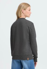Grå hettegenser med rund hals og ribbede mansjetter, med en liten brun etikett i sømmen og en avslappet passform. Bakgrunnen er lys.