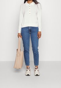 White long-sleeve polo sweater with a button placket, paired with blue jeans and beige tote bag. Sneakers with a white and maroon design.
