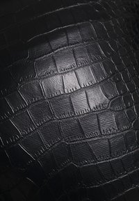 Svart läder med krokodilsmönster som har en slät textur med synliga fjäll och en lätt lyster, vilket framhäver dess strukturerade design.