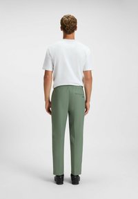 Lysgrønne bukser med en afslappet pasform, der har en elastisk talje og en baglomme. Kombinationen med en ensfarvet hvid t-shirt med korte ærmer.