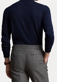 Tummansininen neulepusero pitkähihaisilla hihoilla, yhdistetty harmaisiin räätälöityihin housuihin, joissa on vyöyksityiskohta ja takataskut.