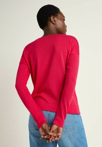 Red long-sleeve sweater made from soft fabric, featuring a relaxed fit and crew neckline, paired with light blue jeans.