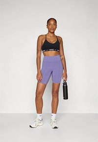 Melns sporta krūšturis ar baltu logotipu, violetas augsta vidukļa šorti, balti sporta apavi un melns ūdens pudele. Gluda, elastīga auduma, pieguloša dizains.