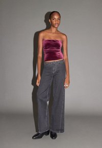 Vínový sametový top bez ramínek s přiléhavým střihem, doplněný tmavě šedými širokými džínami s opaskem zdobeným cvočky a černými kotníkovými botami.