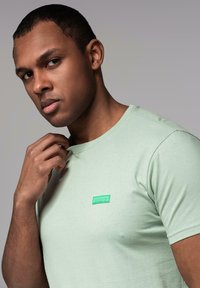 T-shirt in cotone verde menta con scollatura a girocollo, maniche corte e un piccolo patch del logo verde sull'area sinistra del petto.