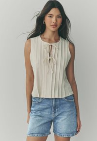 Beige ärmlös topp med lodräta ränder och knytning vid halsen, i kombination med ljusblå denimshorts.