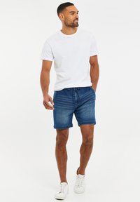 T-shirt bianca in cotone abbinata a pantaloni denim corti con vita regolabile, di colore blu medio e trama sottile, completata da sneakers bianche.