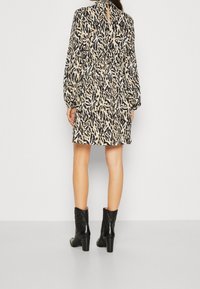 Short-sleeve, knee-length dress with a black and cream leaf pattern, gathered waist, keyhole back, and worn with black heeled ankle boots.