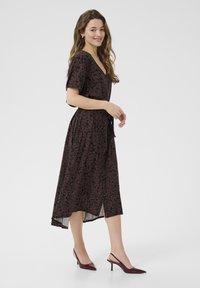 Midi-Kleid mit floralem Muster in dunklem Burgunderrot, kurzen Ärmeln, tiefem V-Ausschnitt, taillierter Taille und asymmetrischem Saum. Kombiniert mit burgunderroten Absätzen.