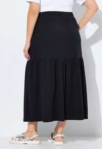 Schwarzer Maxikleid mit einem gestuften Design, elastischem Bund und fließendem Stoff. Kombiniert mit weißen Sandalen mit strukturiertem Muster.