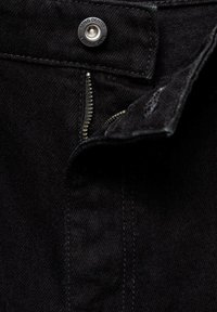 Zwarte denimstof heeft een ritssluiting met een frontknopen sluiting met een metalen afwerking. Zichtbare stiksels voegen detail toe aan het ontwerp.