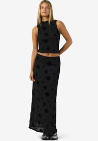 Svart todelt antrekk med ermeløs crop top og lang skjørt. Materialet har et blomstermønster med en gjennomsiktig tekstur.