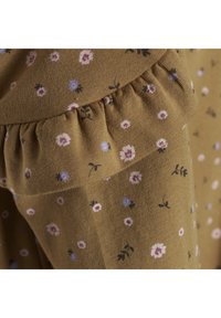Bruine stof met kleine bloemmotieven in roze, paars en blauw, met een geplooide rand aan de naad voor extra textuurdetail.