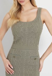 Olivegrøn strikket tanktop med kabelmønstre og en tætsiddende design. Har en bred halsudskæring og ribbet kant med dekorative hardware-detaljer.