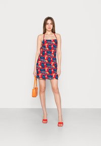Vestido con estampado floral en colores rojo, azul y verde. Presenta tirantes finos y un corte recto. Complementado con accesorios y tacones naranjas.