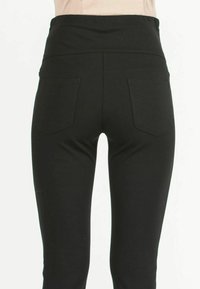 Black leggings made from stretchy material, featuring a high waistband and two back pockets; smooth texture and fitted design.