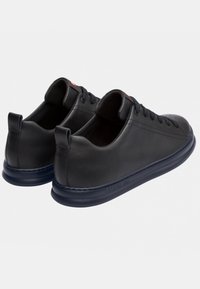 Sneaker in pelle nera con profilo basso, forma arrotondata, design con lacci e suola in gomma testurizzata. Presenta un logo sul tallone posteriore.
