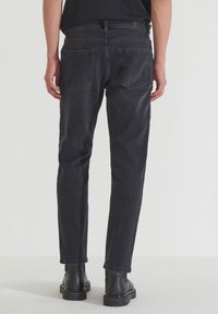 Vaqueros de mezclilla negra con un corte recto, cinco bolsillos, desvanecimiento sutil y costuras en tono, combinados con botines negros.