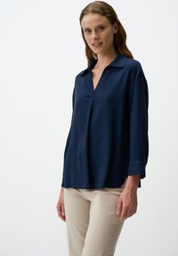 Blusa leggera di colore blu navy, con collo a revers, maniche a tre quarti e taglio rilassato. Presenta una sottile plice frontale.