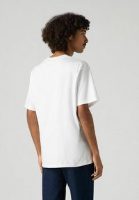 Valkoinen puuvillapaita, jossa on pyöreä pääntie ja lyhyet hihat, esitetty takaa. Pehmeä tekstuuri ja rento istuvuus.