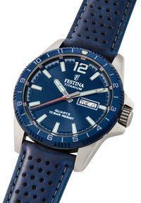 Titano laikrodis su mėlynu ciferblatu ir derančiu perforuotu odiniu dirželiu. Jame yra švytintys valandų žymekliai ir datos langelis 4 valandą.