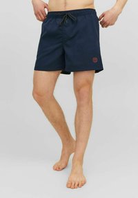 Pantaloni da bagno navy con vita elastica, dettagli con cordino e un logo discreto sul lato sinistro. Tessuto leggero.