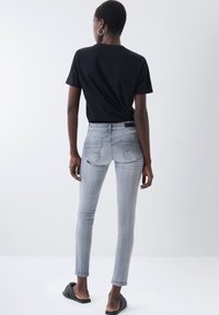 Schmal geschnittene graue Jeans aus Denim mit einem klassischen Fünf-Taschen-Design, kombiniert mit einem schwarzen T-Shirt mit kurzen Ärmeln und schwarzen Slippern.
