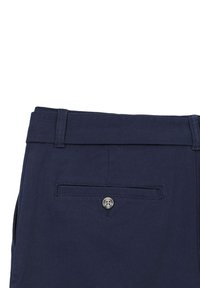 Dettaglio di una tasca posteriore di pantaloni blu navy con chiusura a un bottone e passanti per cintura sulla vita.