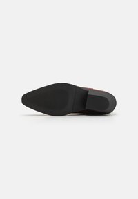 Braunes Wildleder Schuh mit einer schwarzen Gummisohle. Die Sohle ist am Absatz leicht erhöht und besitzt ein strukturiertes Design für besseren Halt.