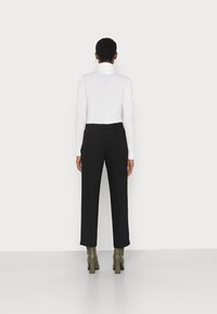 Hvit langermet genser med høy hals, svarte skreddersydde bukser og grønne høyhælede støvler. Outfiten har et minimalistisk design med en slank passform.