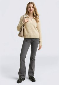 Kremowy sweter na drutach z kołnierzykiem, w połączeniu z szarymi rozszerzanymi dżinsami i czarnymi butami na platformie. Nosi beżową torebkę.