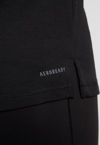 Maglietta sportiva nera AEROREADY con una texture liscia, caratterizzata da una fessura laterale e un logo stampato sull'orlo sinistro inferiore.