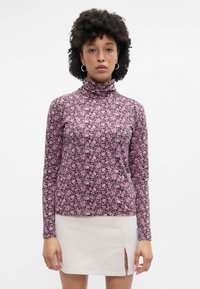 Top de cuello alto de manga larga en púrpura oscuro con un patrón floral rosa; tejido texturizado; combinado con una mini falda beige clara con una abertura lateral.