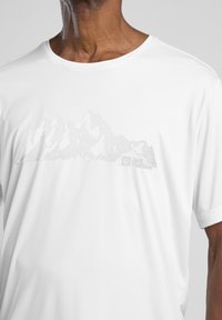 Witte kortärmelige t-shirt met een subtiele grafiek van een bergketen in lichtgrijs en het Jack Wolfskin-logo linksonder.