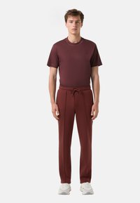 Bordeaux kortekorte T-shirt met reliëflogo, gecombineerd met bijpassende slim fit broek en grijze sneakers. Soepele textuur, casual ontwerp.