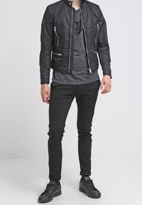 Svart bomberjacka med hög krage, dragkedjefickor och slät yta. Kombinerad med en svart T-shirt och slim fit svarta jeans.