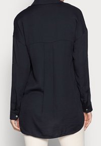 Camicia nera a maniche lunghe con colletto, polsini a bottone, orlo arrotondato e dettaglio sulla schiena. Tessuto morbido con una leggera trama.