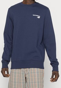 Námořnická modrá mikina vyrobená z bavlněného směsového materiálu, s dlouhými rukávy, kulatým výstřihem a bílým logem "new balance" na hrudi.