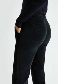 Pantaloni in velluto a coste neri con una vestibilità slim, dotati di tasche laterali e texture liscia. La vista posteriore mostra discrete tasche posteriori e dettagli della vita.