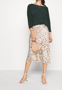 Vihreä teksturoitu neulepusero, valkoinen hame, jossa on ruskea leopardikuvio, yhdistettynä pieneen beigeen käsilaukkuun ja remmikorkokenkiin.