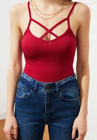 Červený žebrovaný body s tenkými ramínky a křížovým detailem u výstřihu, spárovaný s modrými džínami s vysokým pasem.