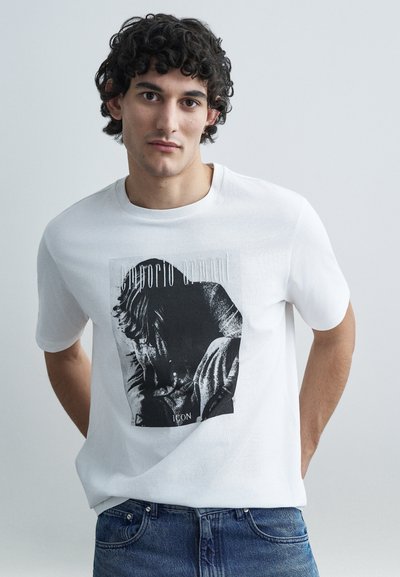 T-shirt en coton blanc arborant une impression graphique en noir et blanc avec un portrait artistique. Col rond et manches courtes.