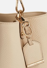 Borsa in pelle beige con superficie testurizzata, hardware dorato e un'etichetta rimovibile con un tocco dorato. Ingrandimento della parte superiore della borsa e della chiusura.