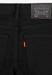 Fekete farmernadrág, slim fit szabással, két hátsó zsebbel és piros címkével kiemelve. A derékrészén egy márkázott bőrpötty található.