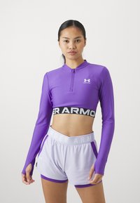 Lilla langermet treningsgenser med halvlukk, kombinert med lyse lilla shorts med en svart-hvit merkebånd i livet.