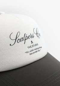 Gorra con una parte superior de algodón blanco, visera gris y nombre de marca bordado. El texto a continuación dice "DISFRUTAMOS HACER COSAS QUE A LA GENTE LE GUSTAN."