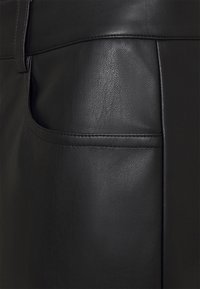 Calças de couro pretas com uma textura suave, design estruturado e um bolso traseiro com um acabamento limpo e detalhes de costura.