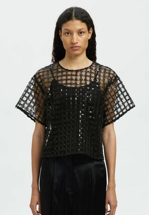 Haut noir à manches courtes en tissu transparent avec un motif en grille et des sequins. Doublure noire unie. Col rond, coupe décontractée.