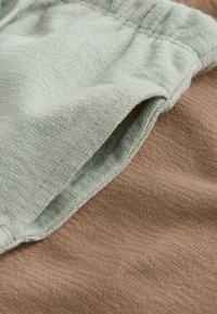 Grüner und brauner Stoff mit sichtbaren Nähten. Das Grün hat eine weiche, frottierartige Struktur; das Braun ist glatt und leicht gerippt.