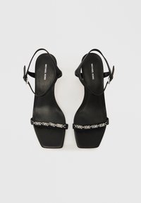 Μαύρα δερμάτινα σανδάλια με τακούνι, τετράγωνη μύτη, λουράκι στον αστράγαλο και διακοσμητική ασημένια αλυσίδα στο μπροστινό μέρος του ποδιού. Σόλα με λογότυπο.